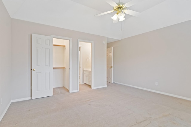 unfurnished bedroom featuring ceiling fan, a spacious closet, ensuite bathroom, light carpet, and a closet