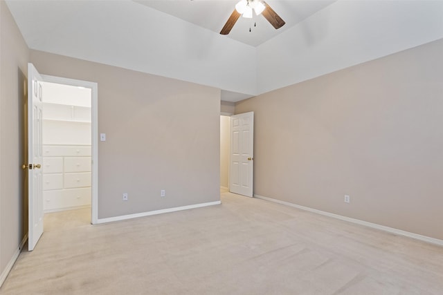 unfurnished bedroom featuring a spacious closet, ceiling fan, vaulted ceiling, light carpet, and a closet