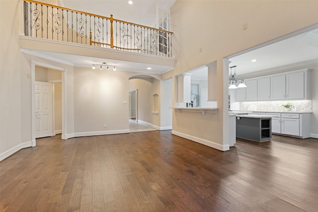 unfurnished living room with an inviting chandelier, a high ceiling, dark hardwood / wood-style floors, and ornamental molding