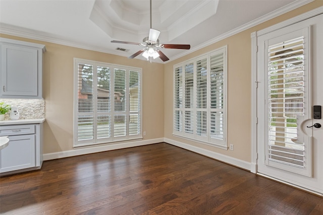 unfurnished dining area featuring ceiling fan, dark hardwood / wood-style flooring, ornamental molding, and a tray ceiling