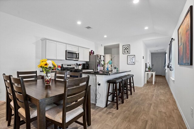 kitchen with white cabinetry, lofted ceiling, a breakfast bar area, appliances with stainless steel finishes, and light wood-type flooring