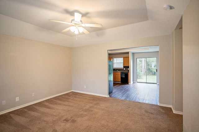 spare room featuring ceiling fan, a raised ceiling, and dark carpet