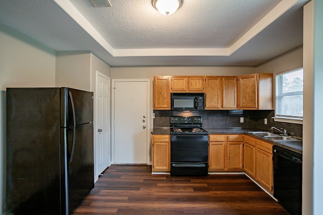 kitchen with black appliances, sink, backsplash, a tray ceiling, and dark wood-type flooring