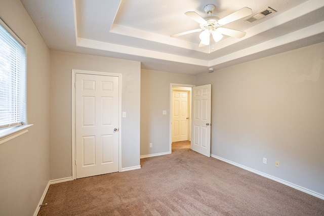 unfurnished bedroom featuring ceiling fan, a tray ceiling, and light carpet