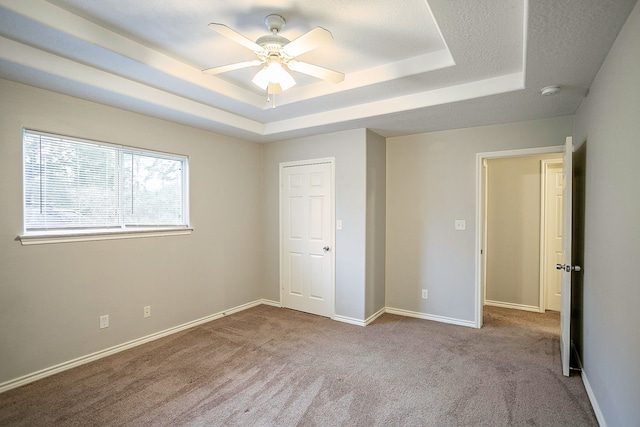 unfurnished bedroom with ceiling fan, a tray ceiling, and light carpet