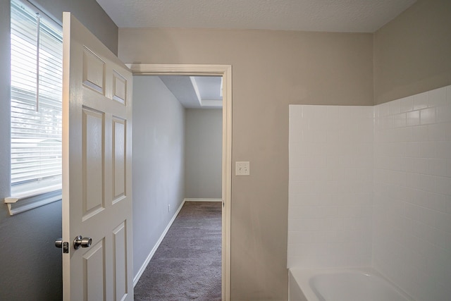 corridor with a textured ceiling and dark colored carpet