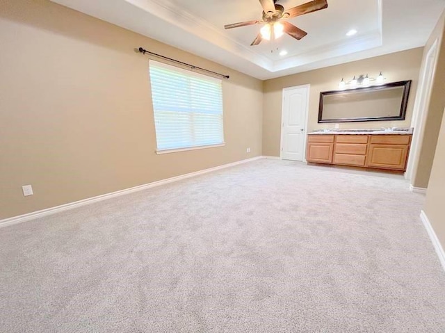 unfurnished bedroom with a raised ceiling, ceiling fan, ensuite bathroom, and light carpet