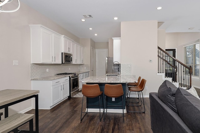 kitchen with kitchen peninsula, decorative backsplash, light stone counters, stainless steel appliances, and white cabinets