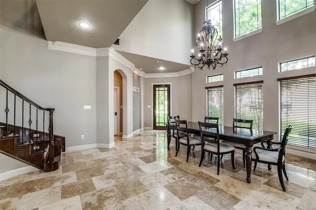 dining area featuring a towering ceiling, plenty of natural light, ornamental molding, and a notable chandelier