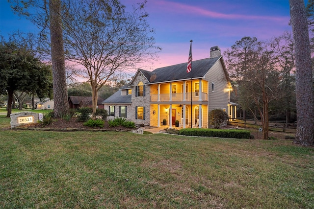 back house at dusk with a balcony and a lawn