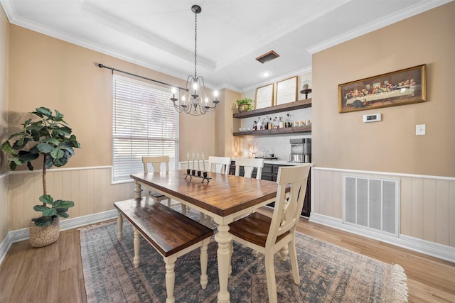 dining space featuring crown molding, a raised ceiling, light hardwood / wood-style flooring, and a notable chandelier