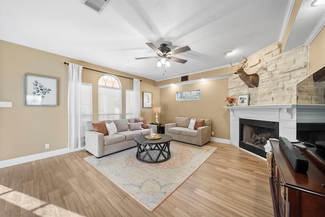 living room with crown molding, ceiling fan, a fireplace, and light wood-type flooring