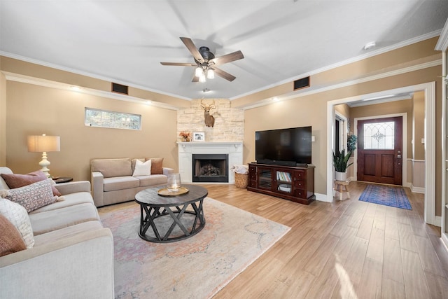 living room with crown molding, ceiling fan, a stone fireplace, and light hardwood / wood-style flooring