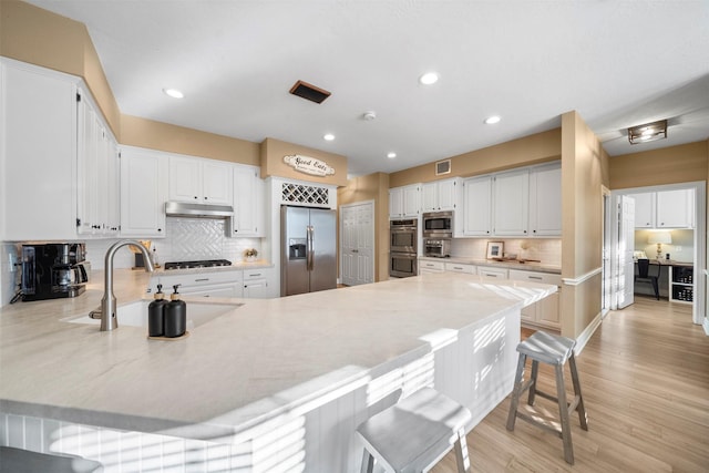 kitchen with a kitchen bar, sink, white cabinetry, stainless steel appliances, and decorative backsplash