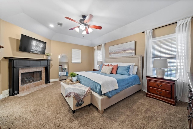 carpeted bedroom with a tile fireplace, a raised ceiling, and ceiling fan