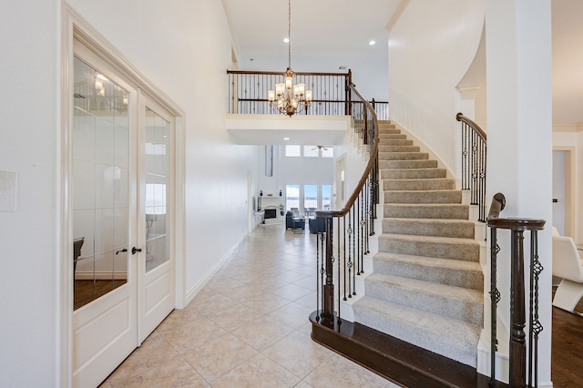 staircase featuring a notable chandelier, ornamental molding, a high ceiling, and french doors