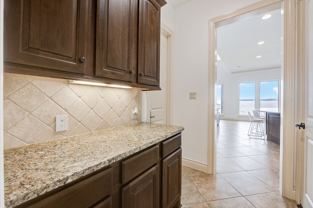 kitchen with tasteful backsplash, dark brown cabinetry, light stone counters, and light tile patterned flooring