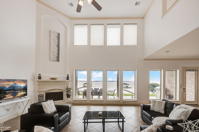 living room with a high ceiling, ceiling fan, ornamental molding, and light tile patterned flooring