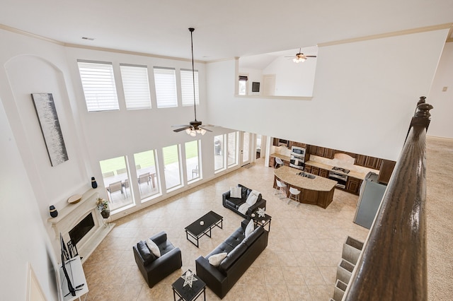 tiled living room with ceiling fan, ornamental molding, and a high ceiling