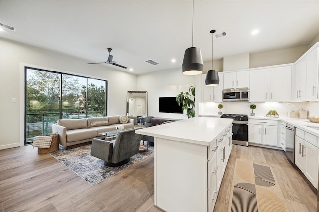 kitchen with white cabinetry, a center island, stainless steel appliances, decorative light fixtures, and light wood-type flooring