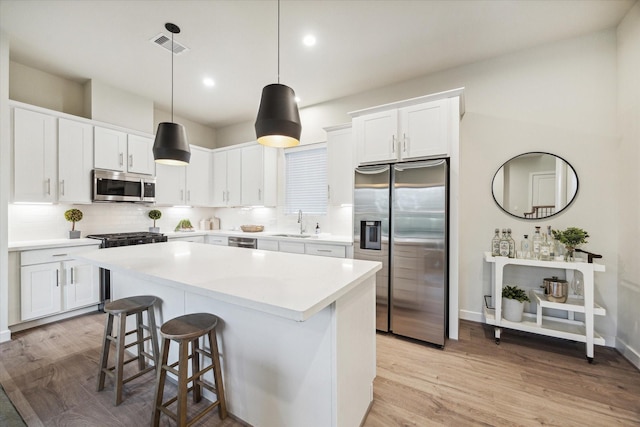 kitchen featuring a center island, sink, decorative light fixtures, white cabinets, and appliances with stainless steel finishes