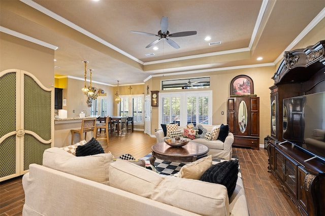 living room featuring ceiling fan with notable chandelier, a tray ceiling, and ornamental molding