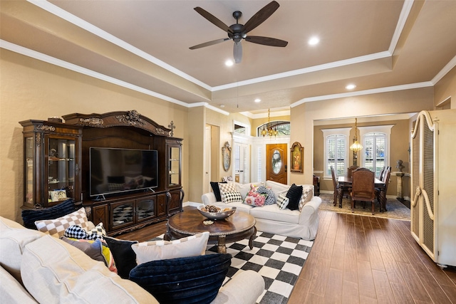 living room with dark hardwood / wood-style floors, crown molding, ceiling fan with notable chandelier, and a tray ceiling