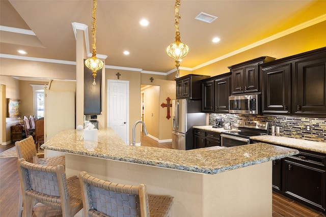 kitchen featuring a kitchen breakfast bar, stainless steel appliances, hanging light fixtures, and dark wood-type flooring