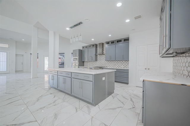 kitchen with pendant lighting, wall chimney exhaust hood, gray cabinetry, and backsplash