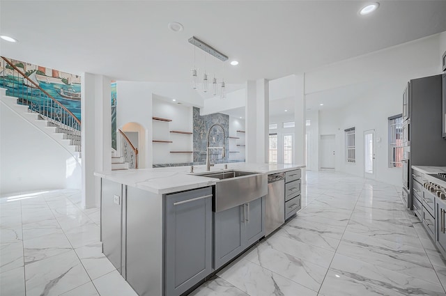 kitchen with light stone countertops, appliances with stainless steel finishes, sink, gray cabinets, and an island with sink