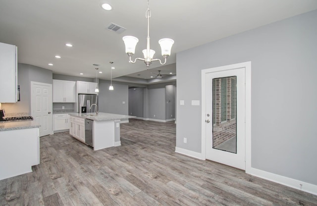 kitchen with a kitchen island with sink, white cabinets, ceiling fan with notable chandelier, decorative light fixtures, and stainless steel appliances