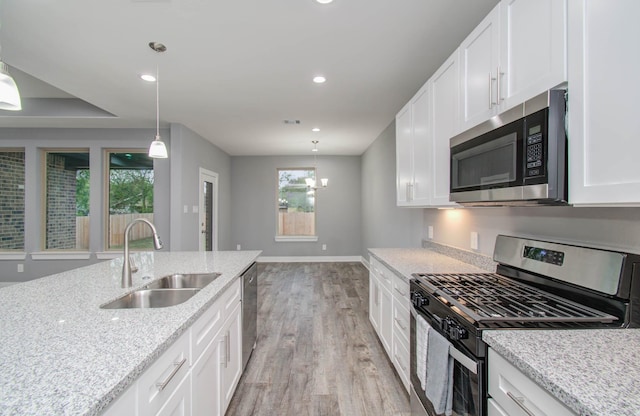 kitchen with sink, hanging light fixtures, light stone counters, white cabinetry, and stainless steel appliances