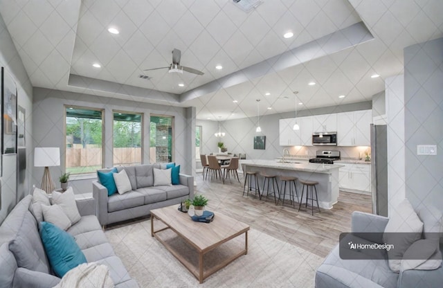 living room featuring a tray ceiling, ceiling fan, and sink