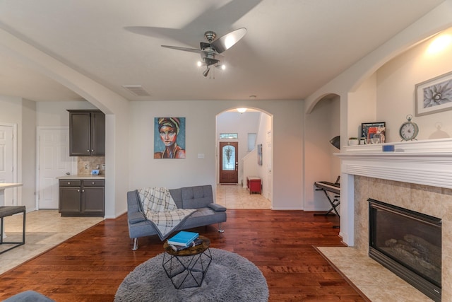 living room featuring a tile fireplace, ceiling fan, and dark wood-type flooring