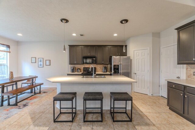 kitchen featuring decorative backsplash, stainless steel appliances, light tile patterned floors, a center island with sink, and hanging light fixtures