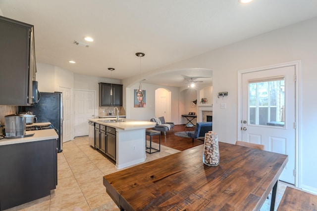 kitchen featuring pendant lighting, sink, decorative backsplash, light tile patterned floors, and an island with sink