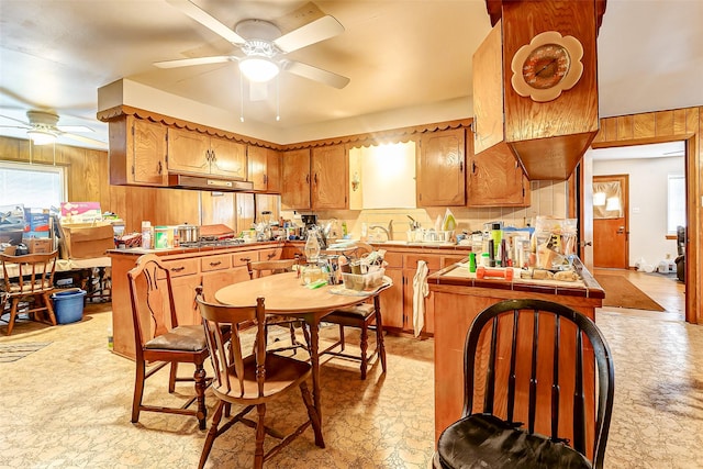 kitchen with kitchen peninsula, wooden walls, ceiling fan, and stainless steel gas cooktop