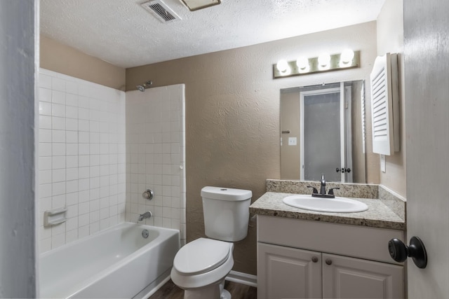 full bathroom with vanity, toilet, a textured ceiling, and tiled shower / bath combo