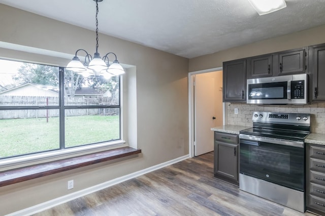 kitchen with light stone countertops, a chandelier, pendant lighting, decorative backsplash, and appliances with stainless steel finishes