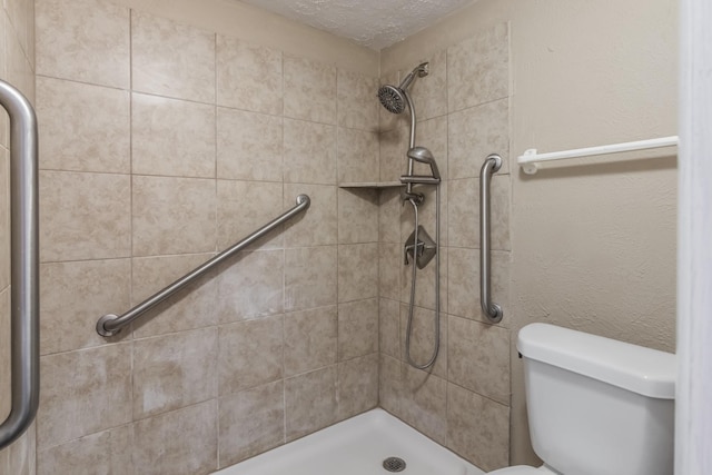 bathroom featuring a textured ceiling, toilet, and tiled shower