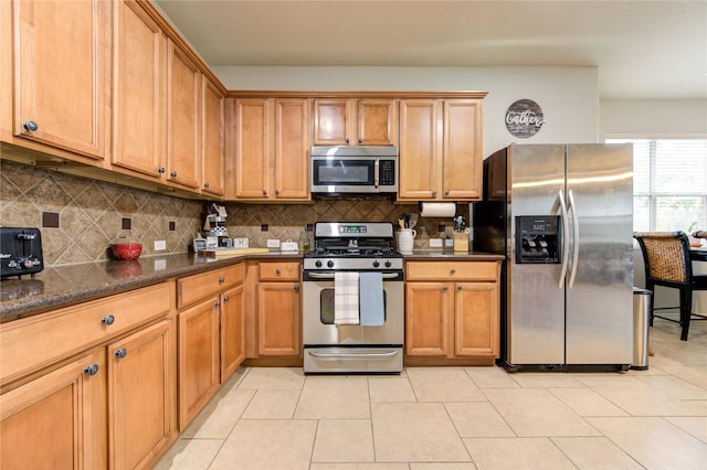 kitchen with decorative backsplash, light tile patterned floors, stainless steel appliances, and dark stone countertops