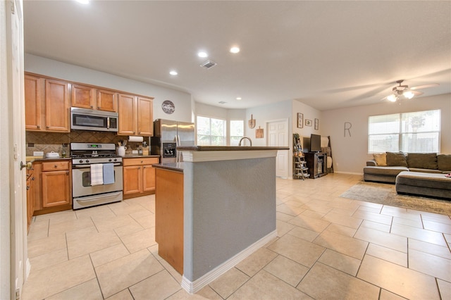 kitchen featuring appliances with stainless steel finishes, tasteful backsplash, a kitchen island with sink, and a healthy amount of sunlight