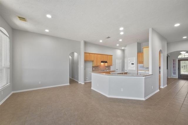 kitchen featuring light tile patterned floors, kitchen peninsula, white microwave, decorative backsplash, and light brown cabinets