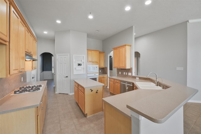 kitchen featuring white appliances, a center island, light brown cabinets, sink, and kitchen peninsula