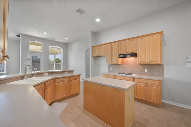 kitchen with light tile patterned floors, tasteful backsplash, light brown cabinetry, a kitchen island, and sink