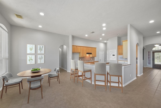 kitchen featuring light tile patterned floors, a kitchen bar, kitchen peninsula, light brown cabinets, and tasteful backsplash