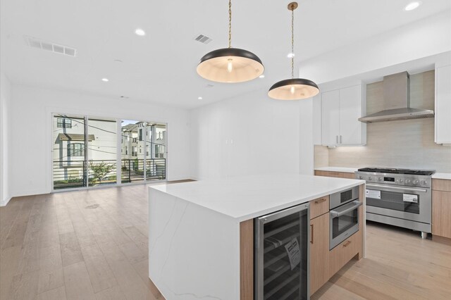 kitchen with appliances with stainless steel finishes, wall chimney exhaust hood, beverage cooler, pendant lighting, and white cabinetry