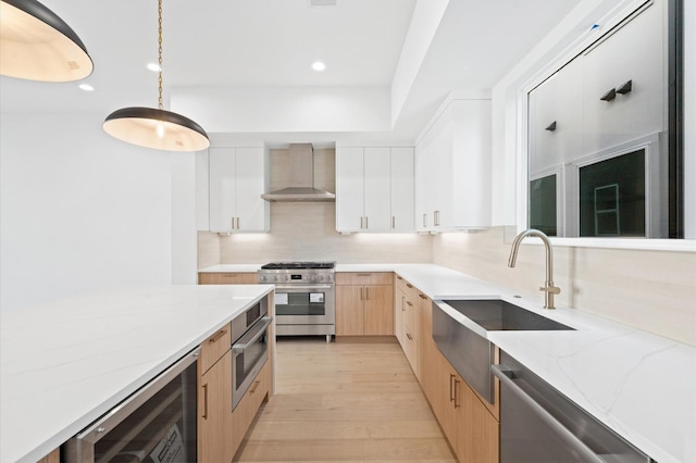 kitchen with wall chimney exhaust hood, decorative backsplash, appliances with stainless steel finishes, decorative light fixtures, and white cabinetry