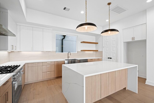 kitchen with stainless steel appliances, a kitchen island, wall chimney range hood, sink, and white cabinetry