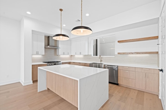 kitchen featuring a kitchen island, sink, wall chimney range hood, dishwasher, and white cabinetry